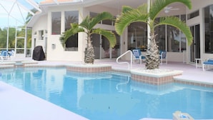 Piscina amb sostre de vidre, palmeres i zona coberta amb seients i cadires.