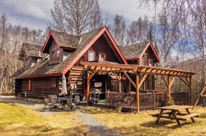A log cabin with a wooden porch and picnic table, surrounded by trees. - Sleeps 16! Moose Lodge Log Cabin and Chalet & Hot Tub (Anchorage)