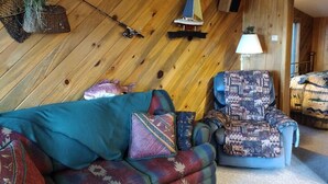 A cozy room with a wooden wall, a sofa, a patterned armchair, a small sailboat model, and a welcome sign. - Lakefront Romantic Getaway - The Little Blue Cabin (Westwood)