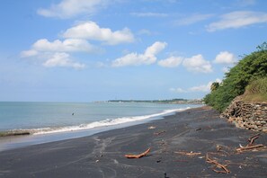 A beach with a black sand shore, a stone wall, and a clear sky.