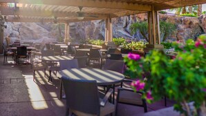 An outdoor patio with round tables and chairs, a rock wall backdrop, and potted plants. - Walking Distance from Coachella and Stagecoach festivals (Indio)