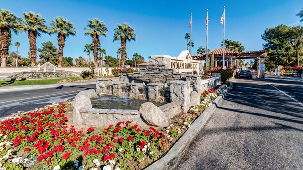 A stone fountain with a sign reading "INDIAN PALMS C.C." surrounded by red flowers and palm trees. - Walking Distance from Coachella and Stagecoach festivals (Indio)