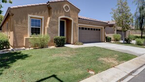 A single-story house with a garage, a front door, and a small front yard with a lawn and a few bushes. - Walking Distance from Coachella and Stagecoach festivals (Indio)
