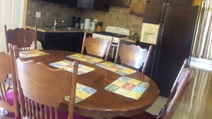 Zona pranzo con tavolo e sedie in legno, in secondo piano una cucina con mobili e elettrodomestici scuri.