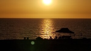 Tramonto sull'oceano con la sagoma di un ombrellone e sedie da spiaggia.