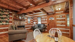 A cozy log cabin interior with a wooden dining table, two sofas, and a fireplace. - Hearts Bursting with Love  Romantic Creekside Retreat!! (Cosby)