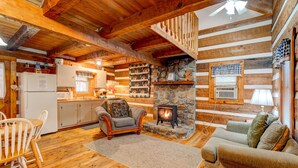 A cozy log cabin interior with a stone fireplace, wooden floors, a dining area, and a staircase. - Hearts Bursting with Love  Romantic Creekside Retreat!! (Cosby)