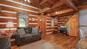 A cozy log cabin interior with a sofa, a television, and a staircase leading to an upper level. - Hearts Bursting with Love  Romantic Creekside Retreat!! (Cosby)