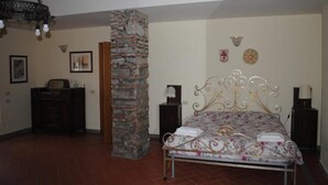 A bedroom with a bed, a stone pillar, a chandelier, and a dresser.