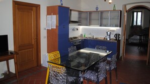 A compact kitchen with a glass dining table, blue cabinets, and a wooden door. - A comfortable apartment in the Tuscan countryside next to the city center. (Firenze)