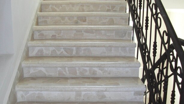 Un escalier avec des marches en pierre et une rampe en fer forgé noir.