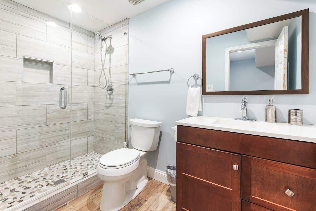 A modern bathroom with a glass-enclosed shower, a white toilet, and a wooden vanity with a mirror.