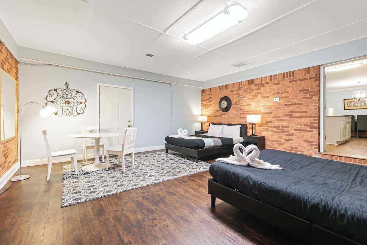 A hotel room with a bed, a desk, a chair, a small table, and a wall clock.