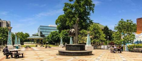 A public square with a central sculpture, benches, and trees.