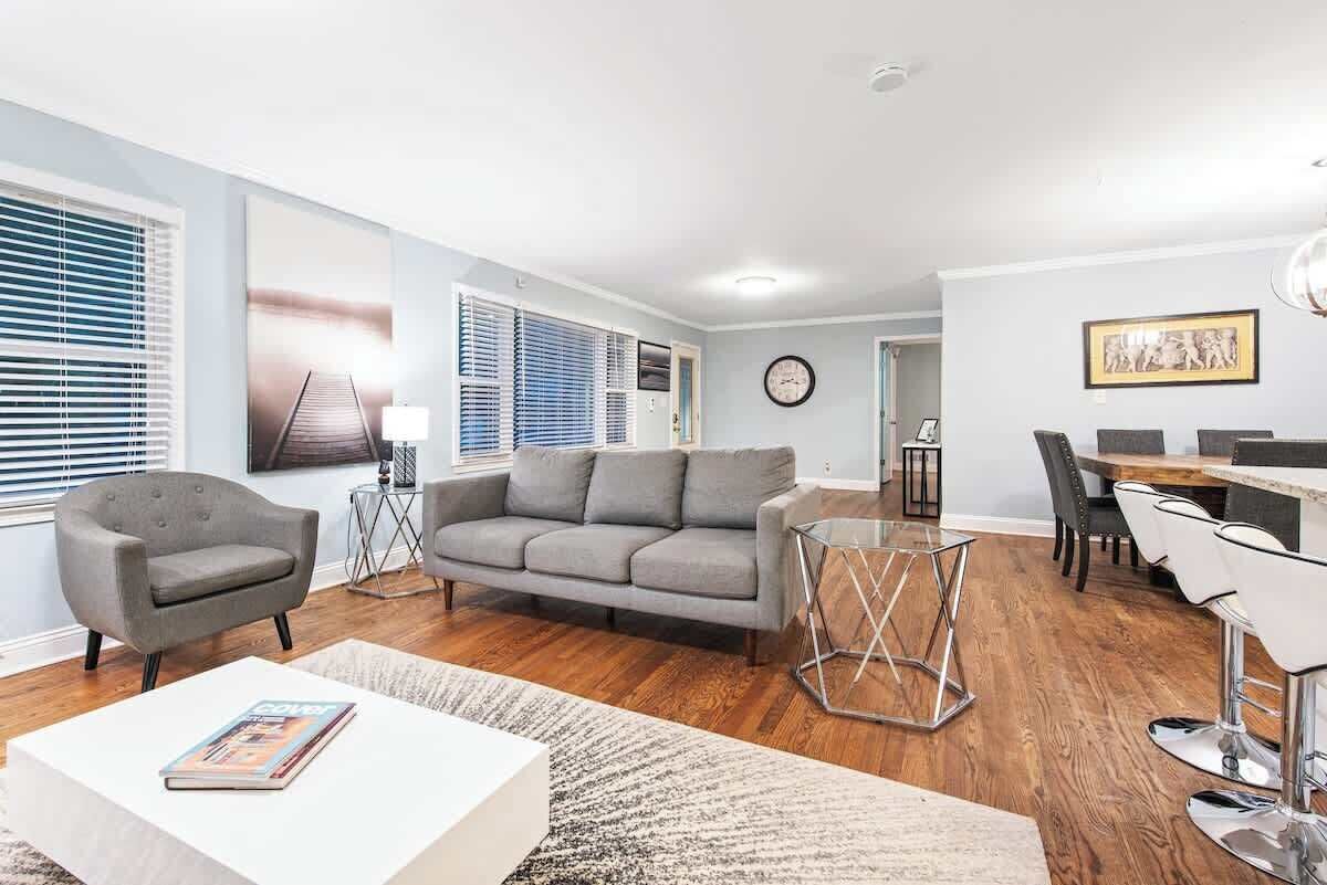 A modern living room with a sofa, armchairs, a coffee table, and a dining area with chairs and a table.