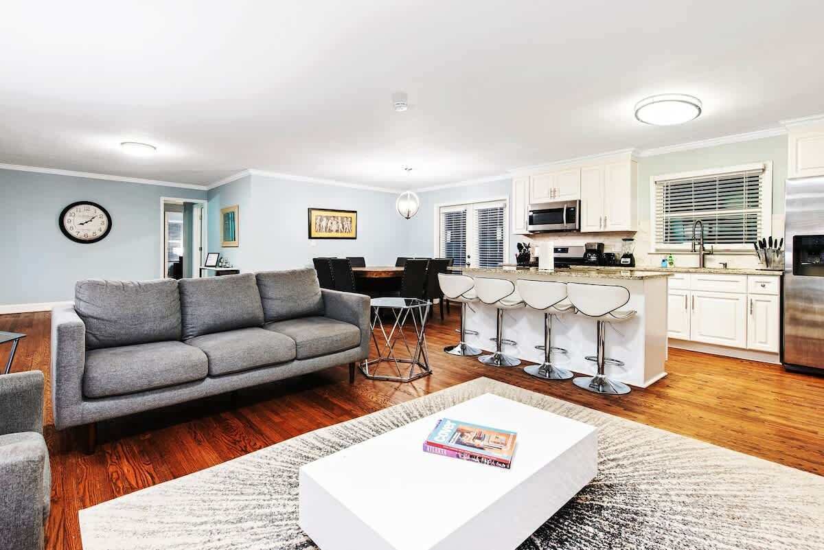 A modern living room with a grey sofa, a white coffee table, and a dining area with bar stools.