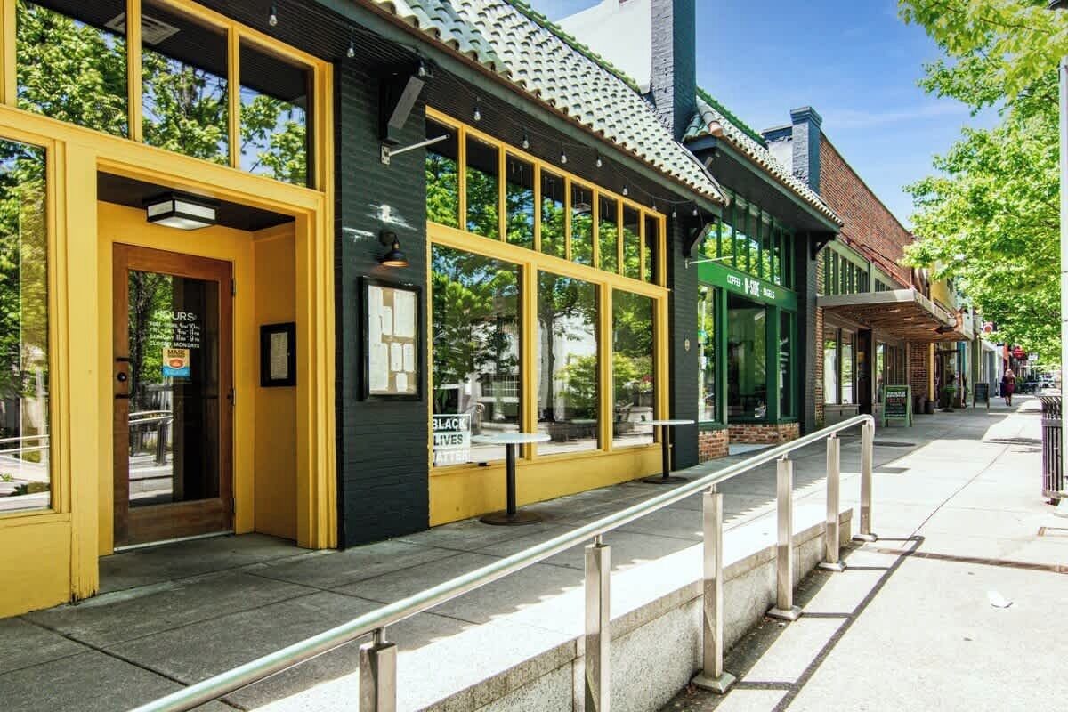 Een gebouw met grote ramen, een gele deur, een zichtbaar bord en een stoep met een leuning.