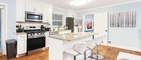A modern kitchen with white cabinets, stainless steel appliances, and a central island with bar stools.