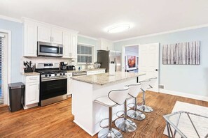 A modern kitchen with white cabinets, stainless steel appliances, and a central island with bar stools.