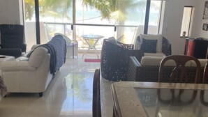 Uma sala de estar moderna com uma mesa de vidro, sofás brancos e vista para a praia.