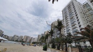 Uma praia com edifícios altos, palmeiras e guarda-sóis.