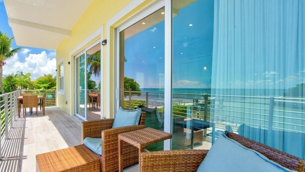 A balcony with wicker furniture, a glass door leading to a pool area, and a view of the ocean.