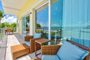 Een balkon met rieten meubilair, een glazen deur naar een zwembad en uitzicht op de oceaan.