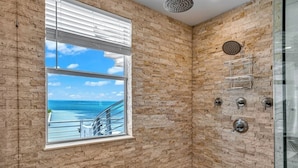 A corner bathroom with a view of the sea through a window, a shower with a rain showerhead, and a glass shower enclosure.