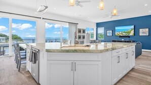 A modern kitchen with a large island, white cabinets, and pendant lighting.