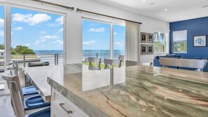 A modern kitchen with a large island, large windows, and a view of the ocean.
