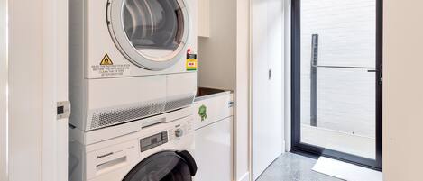 A compact laundry area with a front-loading washing machine, a dryer, and a small trash bin.