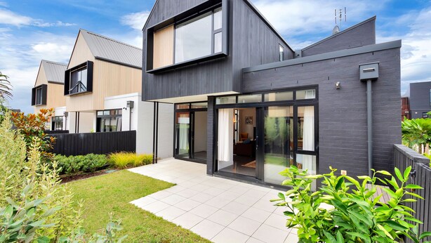 Une maison moderne à deux étages, dotée d’une grande porte d’entrée en verre, d’un espace de vie bien visible et d’un jardin bien entretenu.