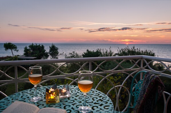A table with two glasses of beer, a candle, and an open book, overlooking a sunset over the sea. - Beachfront Villa Meliti (Kerkyra)