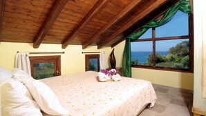 A bedroom with a large bed, two windows with curtains, and a view of the sea.