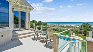Een balkon met glazen hekwerk met uitzicht op een strand en de oceaan.