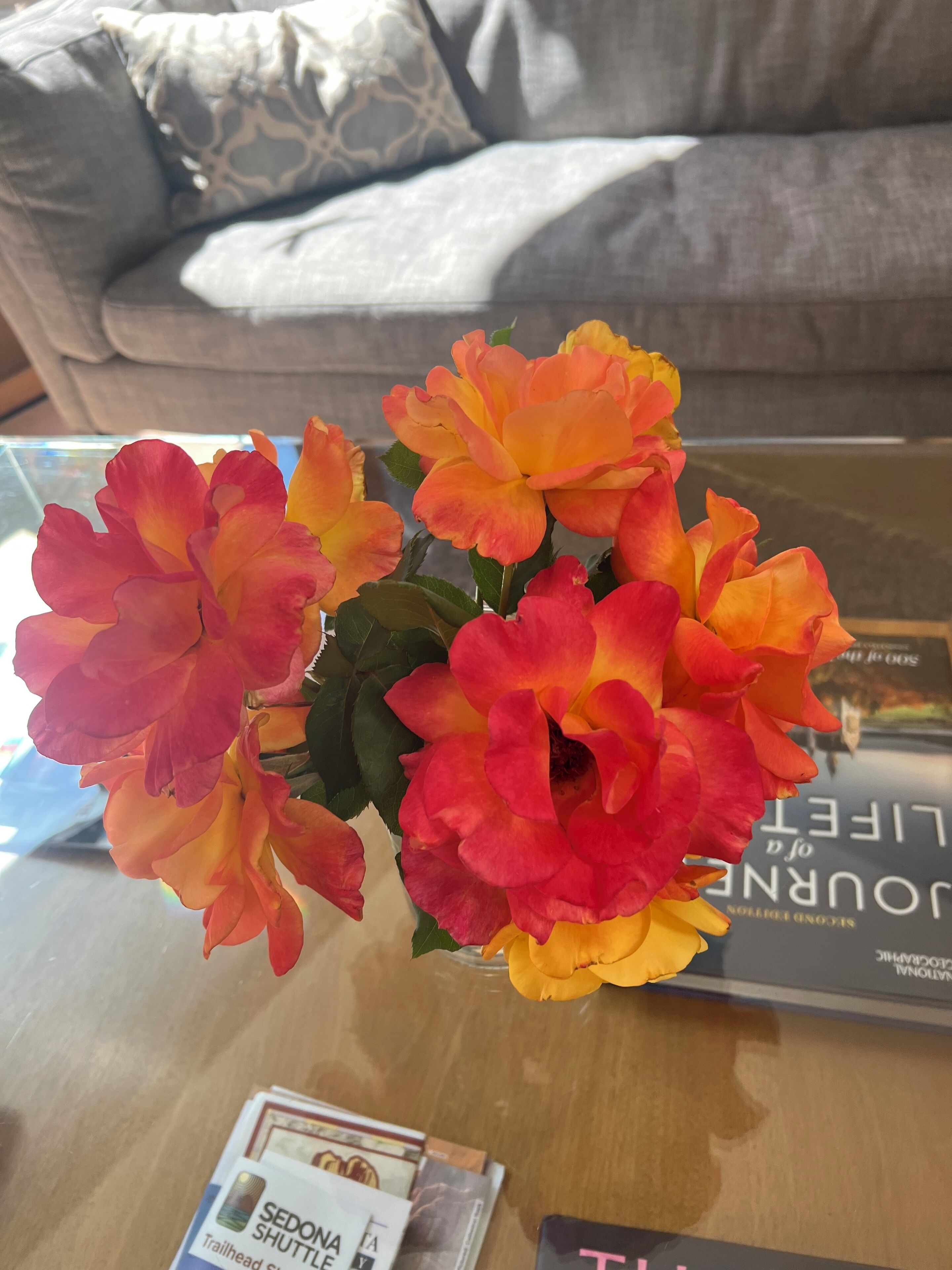 A glass table with a vase of flowers, a book, and a brochure.