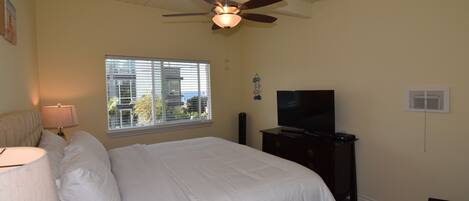 A bedroom with a bed, a ceiling fan, a TV, a window, and a dresser.