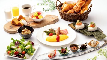 Una variedad de platos que incluyen sushi, cruasanes y una ensalada, dispuesta sobre una mesa blanca.