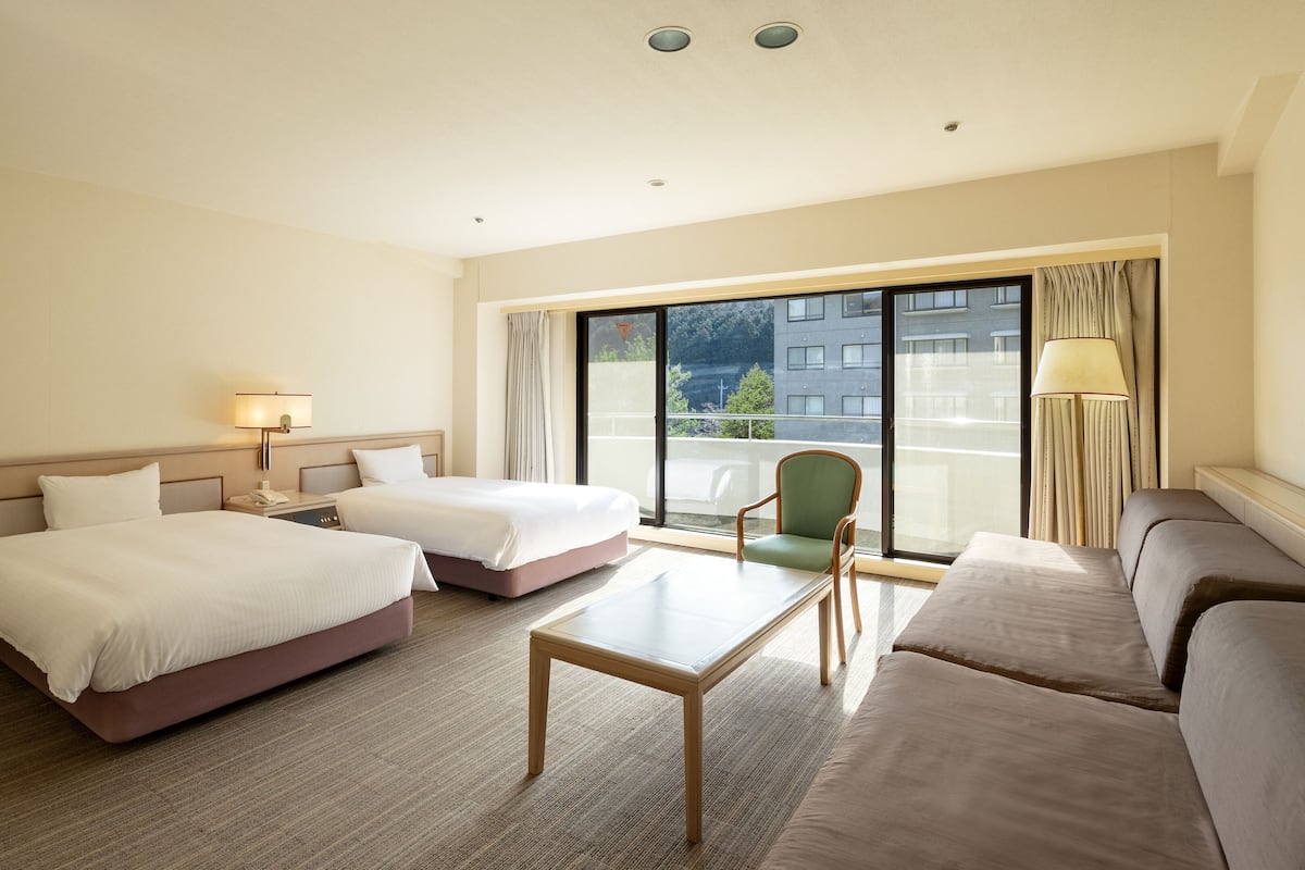Habitación de hotel con dos camas, un sofá, una mesa y un balcón con vistas a edificios.