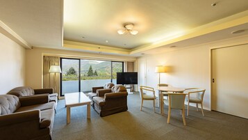 Habitación de hotel con balcón, televisión de pantalla plana, mesa de comedor con sillas y sofá.
