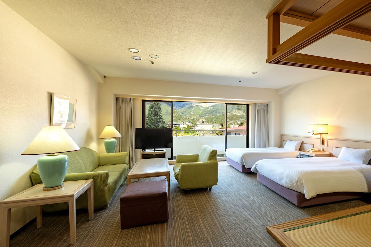 Habitación de hotel con dos camas, un sofá, una televisión y un balcón con vistas a la montaña.