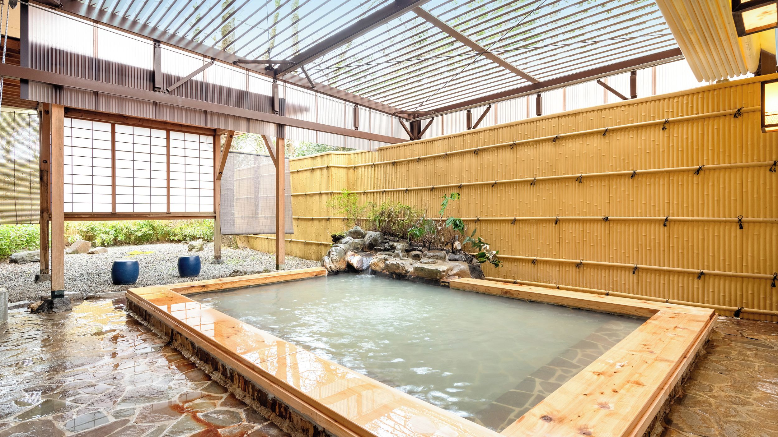 A traditional Japanese onsen with a wooden bath, a bamboo wall, and a view of the surrounding garden.