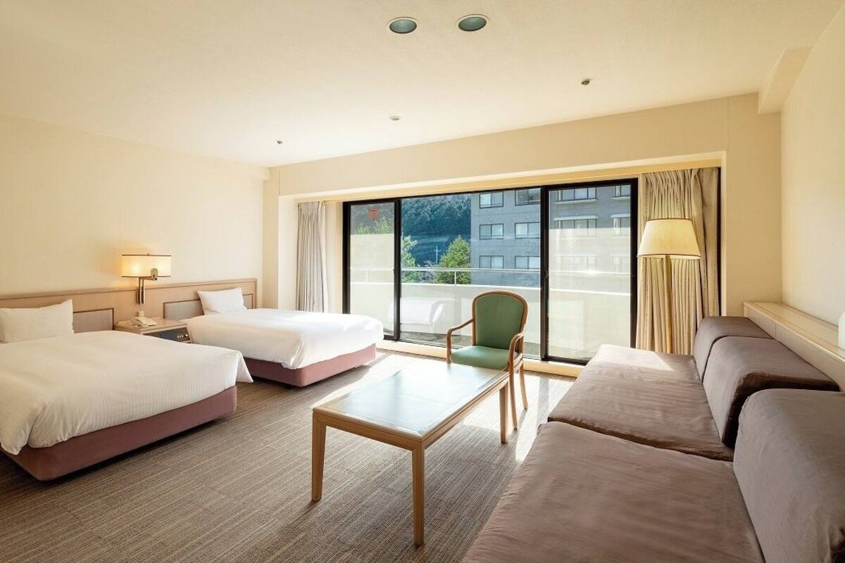 Habitación de hotel con dos camas, un sofá, una mesa y vistas al exterior.