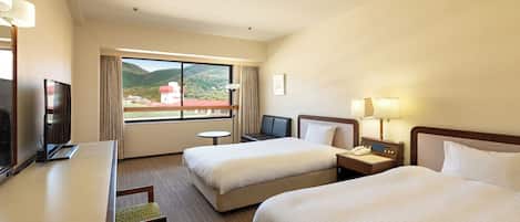 Een hotelkamer met twee bedden, een bureau met een televisie, een klein tafeltje en uitzicht op bergen.