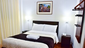 Ein ordentlich gemachtes Bett mit weißer und brauner Bettwäsche, ein kleiner Nachttisch mit Telefon und ein Gemälde an der Wand.