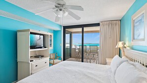 A hotel room with a bed, a television, a desk, and a balcony with a view of the ocean. - Sunset Jetty View! Enjoy one free beach chair set up and umbrella each day! (Destin)