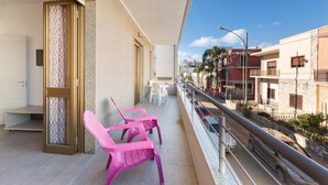 Un balcón con sillas rosadas, una puerta blanca y vista a la calle.