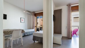 Habitación con cama, escritorio y silla. Tiene una ventana con cortinas, un televisor en la pared y una puerta que da a otra habitación.