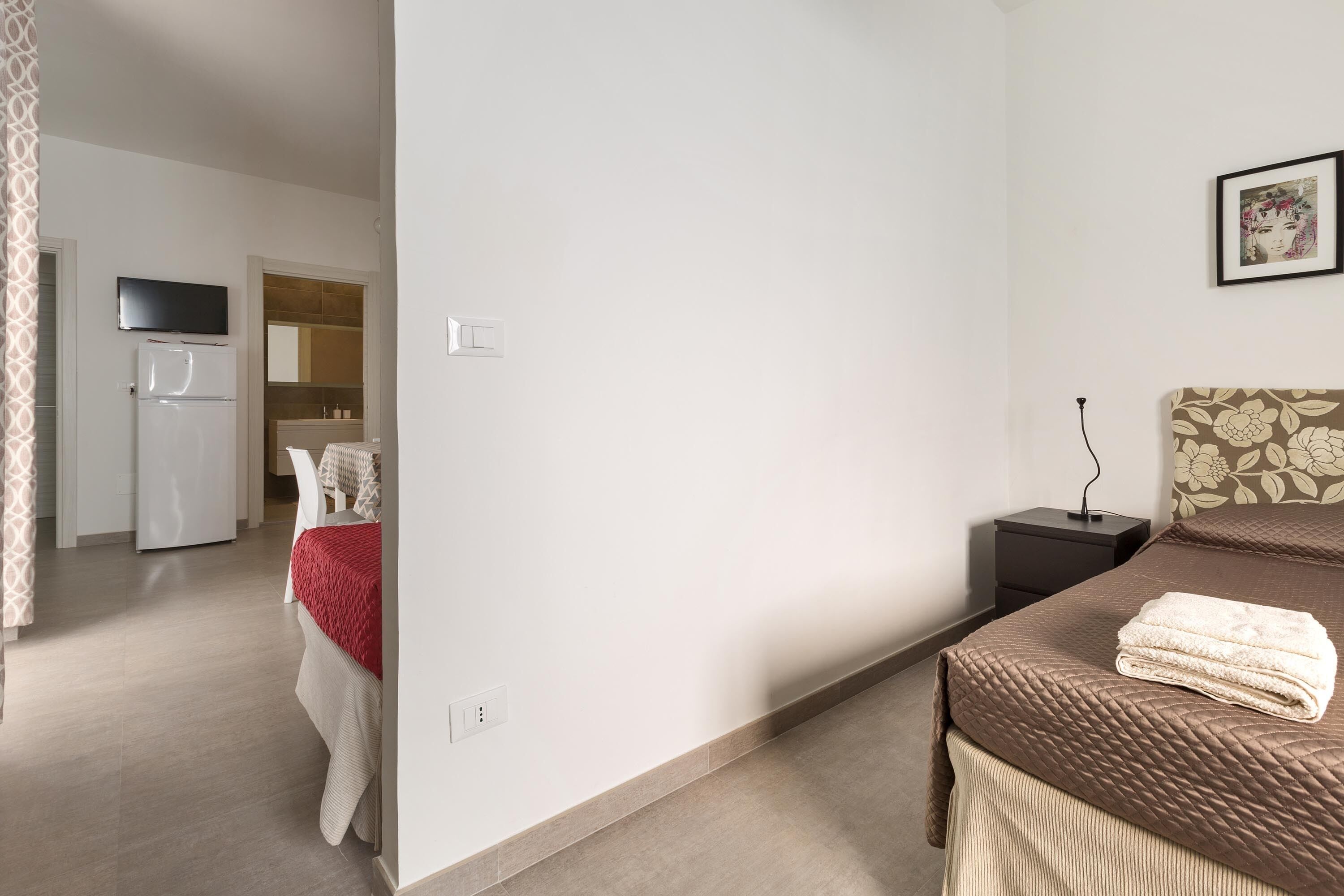 A bedroom with a bed, bedside table, and a TV mounted on the wall.