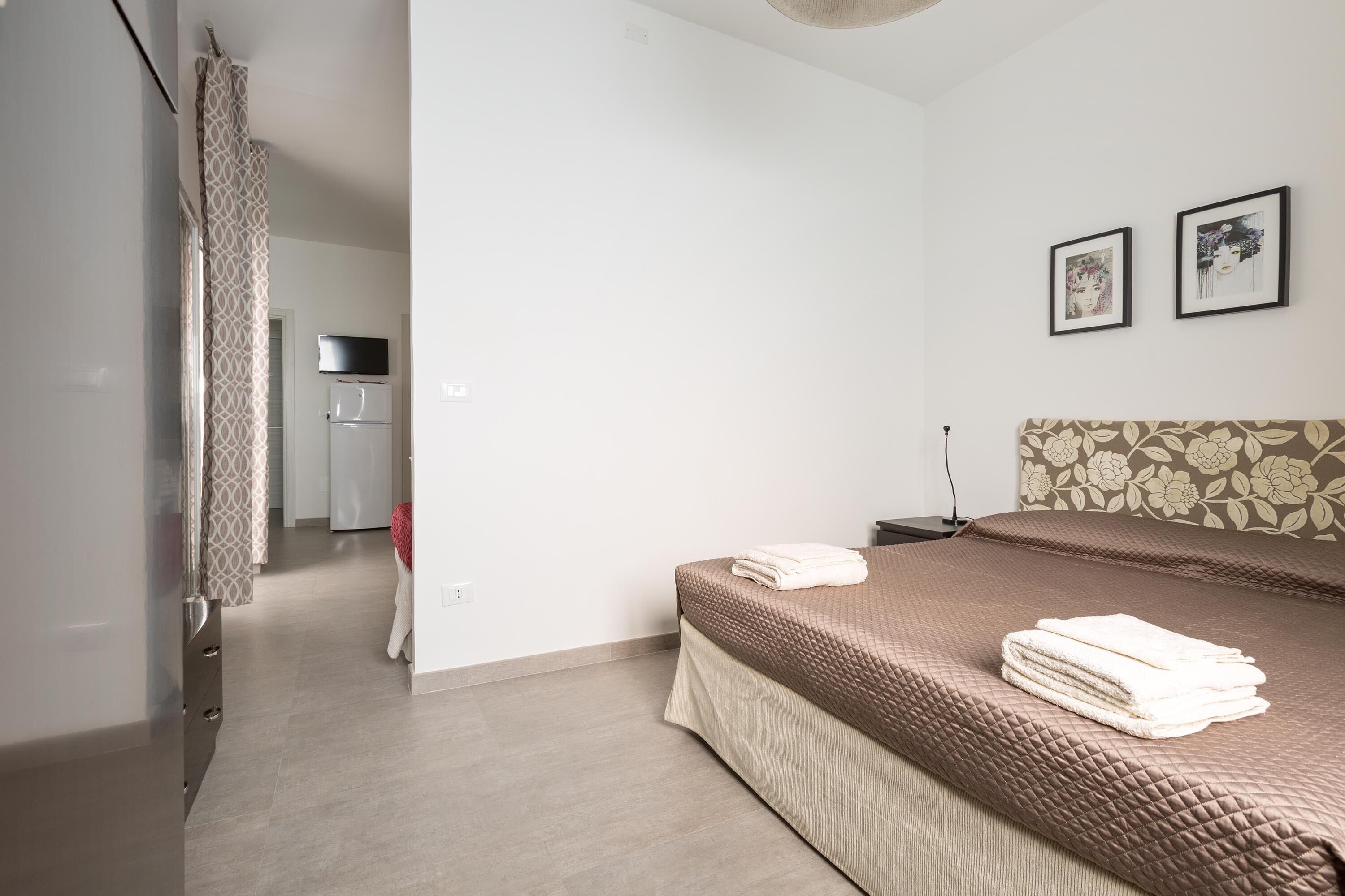 Un dormitorio con una cama, una mesita de noche, una lámpara y un televisor montado en la pared.